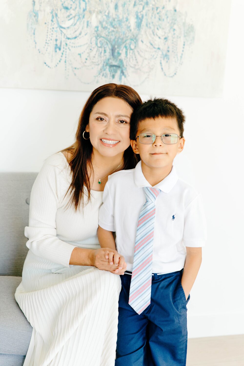 Sandy, who runs Prodigy Montessori, smiling and seated on a sofa with her arm around a young boy in a white polo shirt and striped tie.